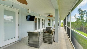 A covered outdoor area with wicker furniture, ceiling fans, and a TV mounted on the wall. - Paddle, Bike & Relax! Canal-front Cape Coral Home (Cape Coral)
