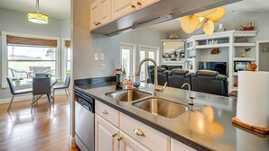 A modern kitchen with stainless steel appliances, a double sink, and a dining area with a glass table and chairs. - Paddle, Bike & Relax! Canal-front Cape Coral Home (Cape Coral)