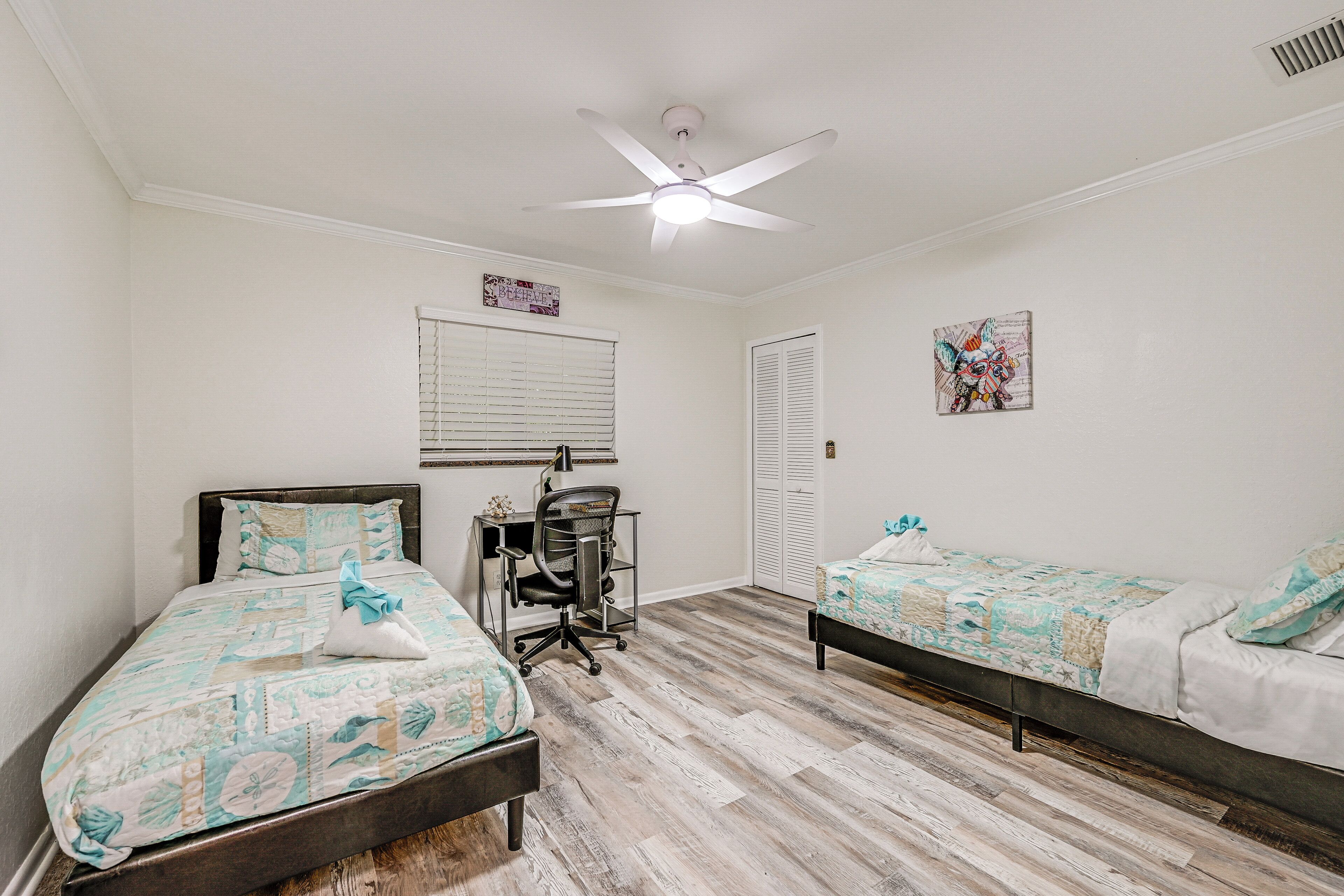 A bedroom with two beds, a desk, and a ceiling fan.