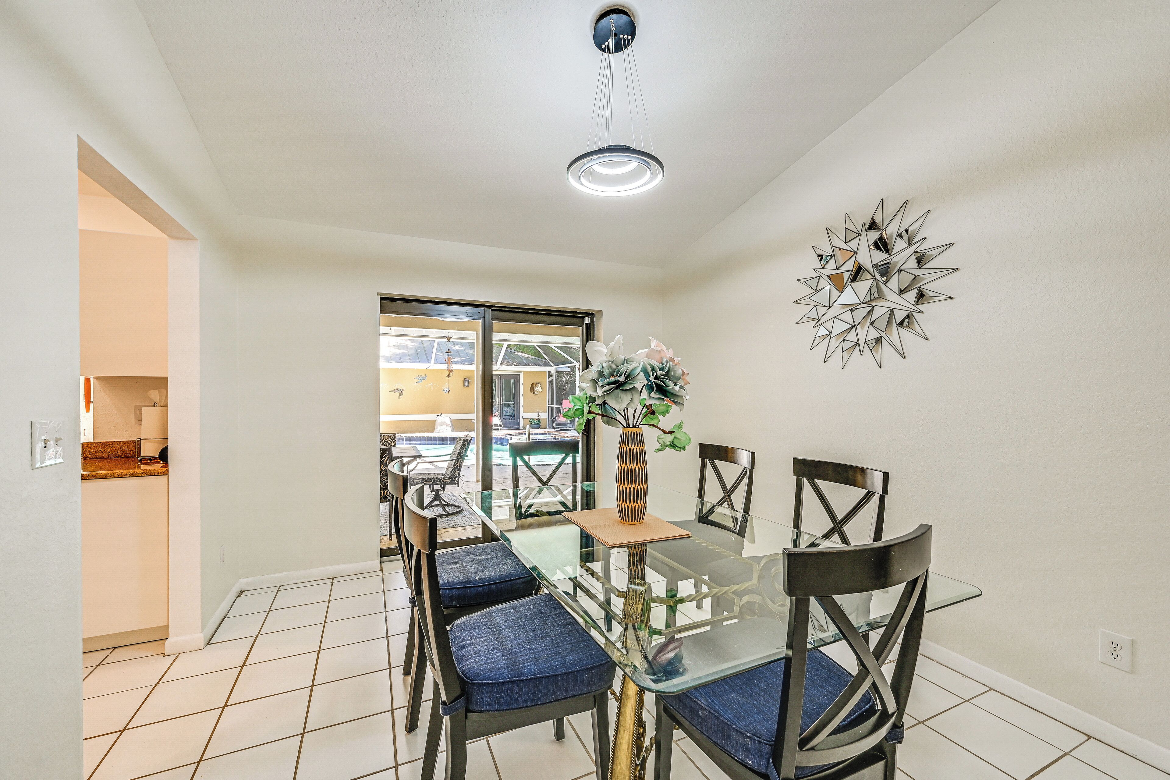 Un coin repas avec une table en verre, des chaises rembourrées bleues, un vase avec des fleurs et un élément décoratif géométrique sur le mur.