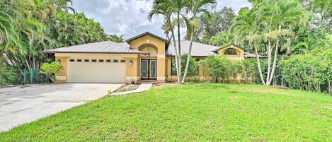 A two-story house with a garage, surrounded by lush greenery and palm trees.