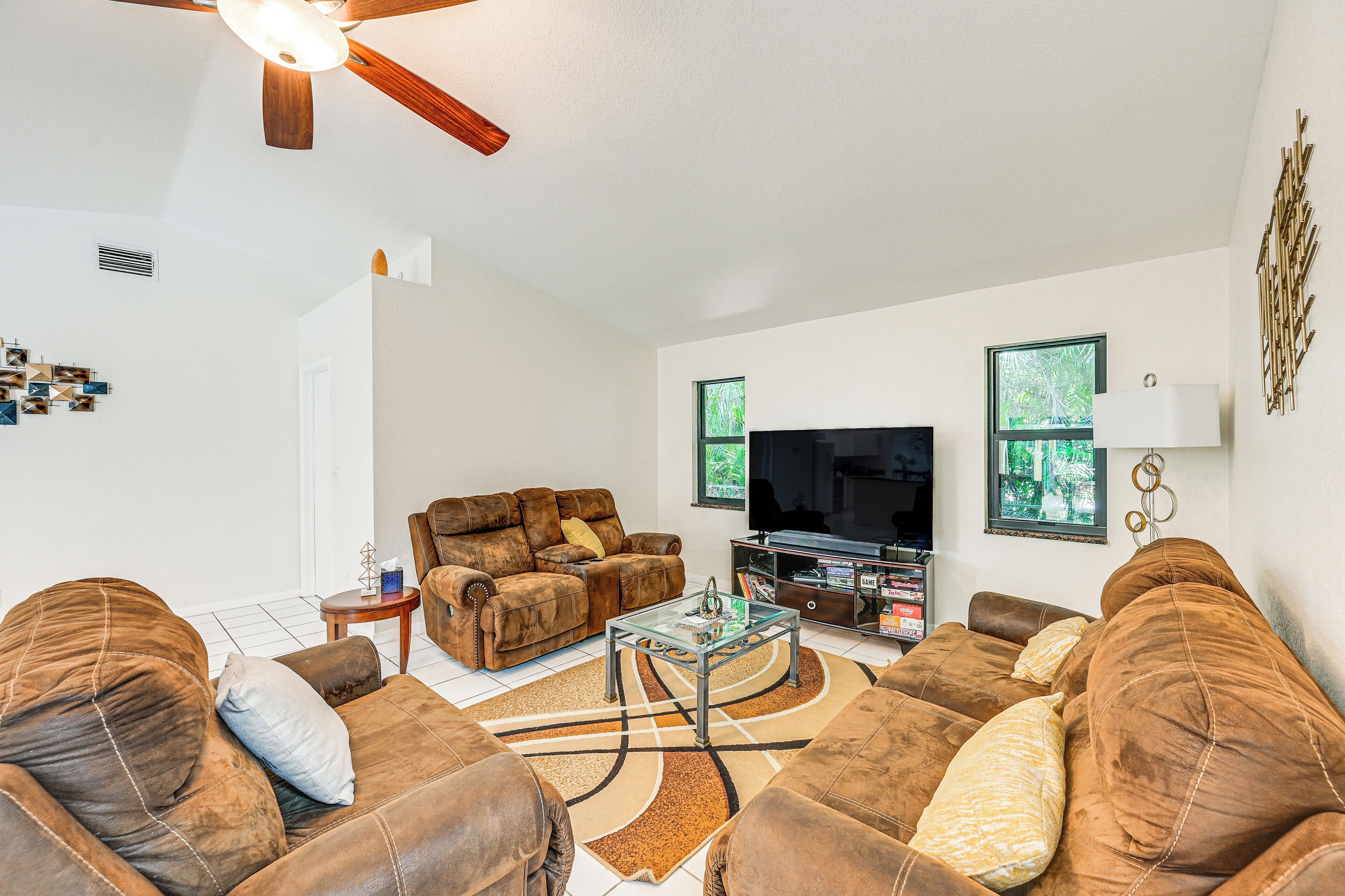 A living room with a brown leather sofa set, a glass coffee table, a flat-screen TV, and a ceiling fan.