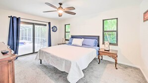 A bedroom with a bed, a ceiling fan, a nightstand, a desk, and a view of a patio through a sliding glass door. - Lovely Naples Home: Backyard Oasis w/ Pool! (Naples)