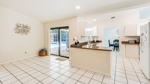 A modern kitchen with a central island, white tiled flooring, and a view to the outside. - Lovely Naples Home: Backyard Oasis w/ Pool! (Naples)