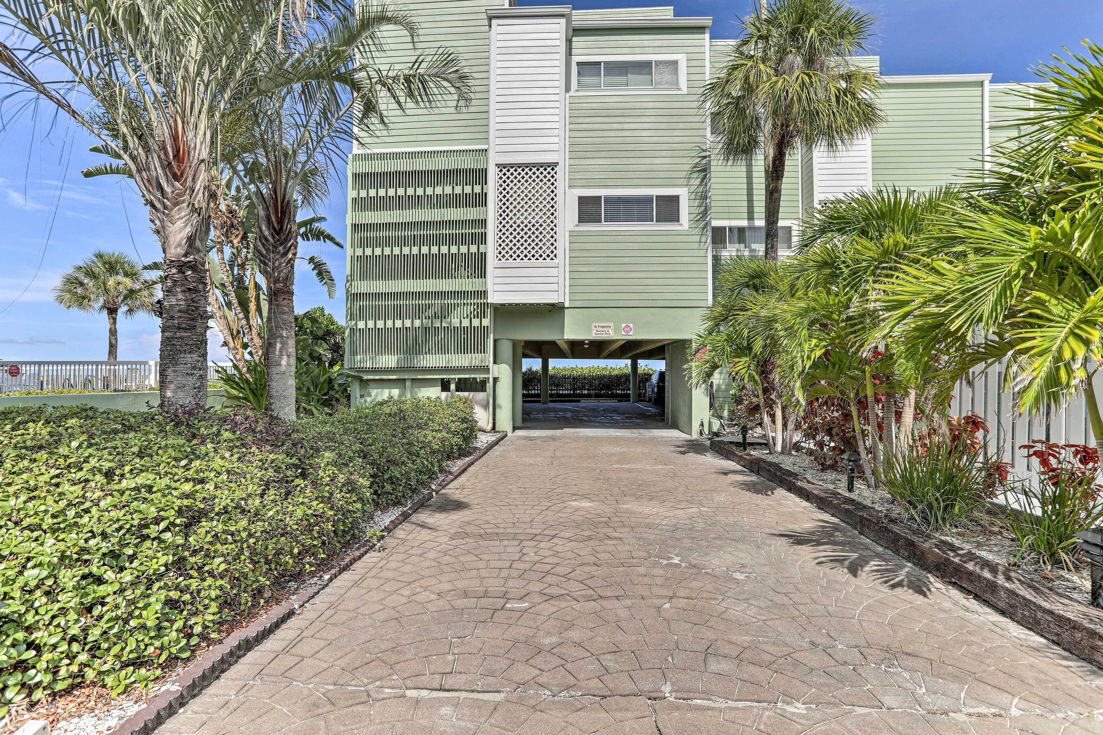 A building with a green facade, a paved entrance, and surrounding palm trees.