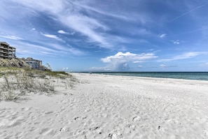 A sandy beach with footprints, a clear sky, and a building on the left.