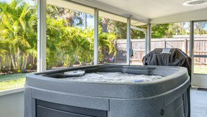 Ett bubbelbad i ett avskärmat utomhusområde med stora fönster och utsikt över en trädgård med palmer.