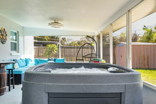 A hot tub in a covered outdoor area with a blue sofa and a wooden fence in the background.