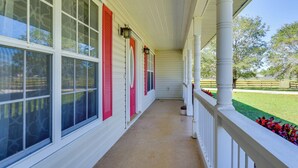 A covered porch with white columns and red shutters, leading to a lawn area. - Private Estate on 10 Acres w/ Pool in Bradenton (Bradenton)