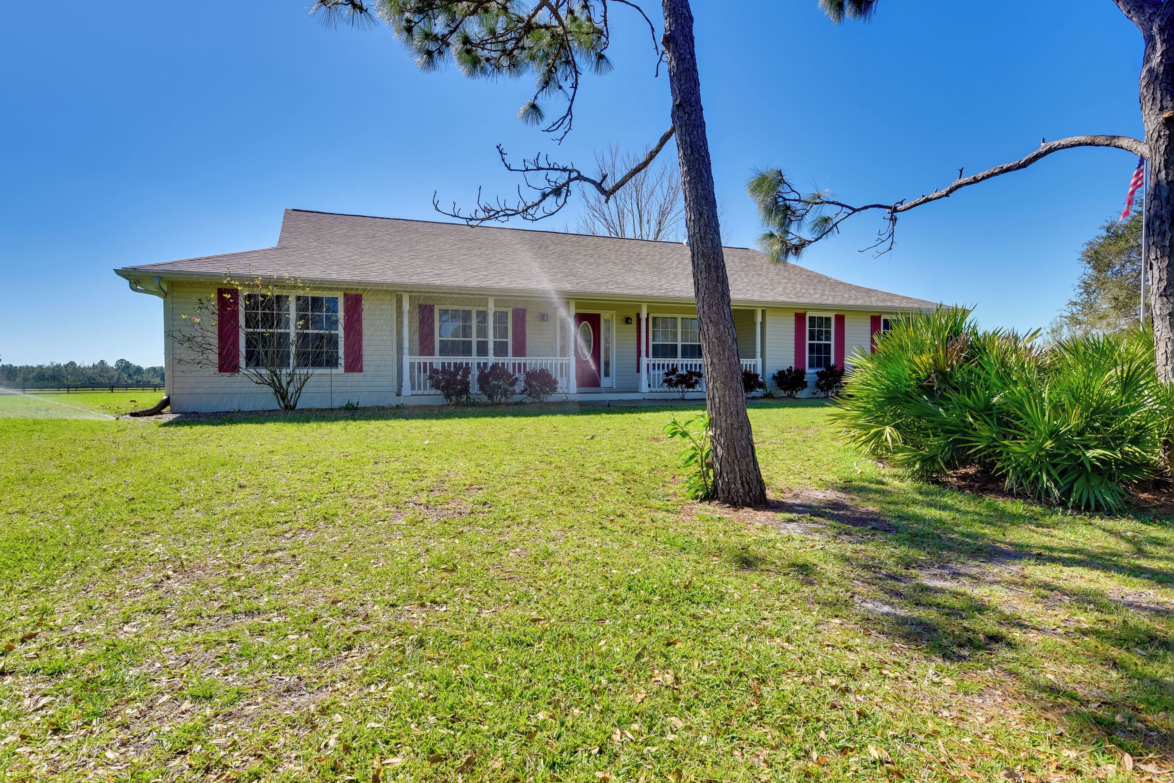 A single-story house with a front porch, a lawn, and a tree.