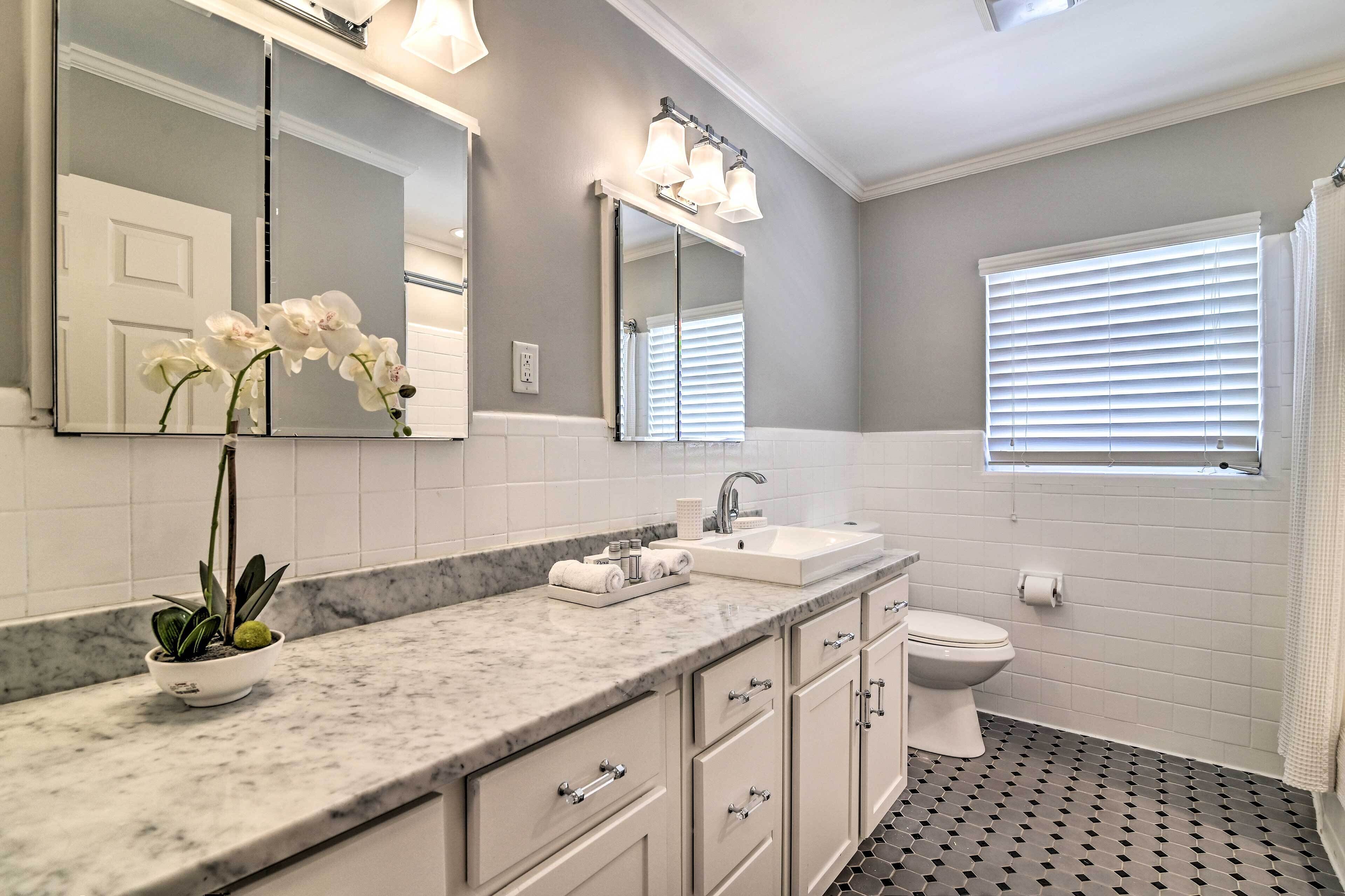 A bathroom with a marble countertop, a sink, a toilet, and a window with blinds.