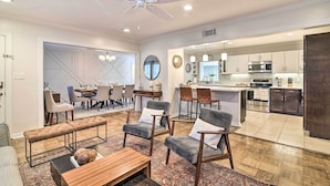 A spacious living room with a large sofa, a coffee table, and a dining area with chairs and a table. A kitchen is visible in the background with modern appliances and cabinets. - Mid-century Modern Escape in Central Lakeland! (Lakeland)
