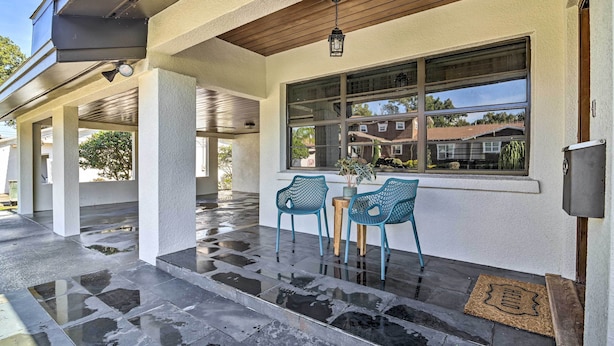 A covered patio area with two blue chairs, a small table, and a potted plant. - Mid-century Modern Escape in Central Lakeland! (Lakeland)