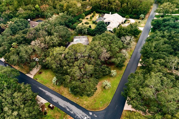 Vista aérea de una zona residencial con una carretera curva, abundante vegetación y una casa grande con techo inclinado.