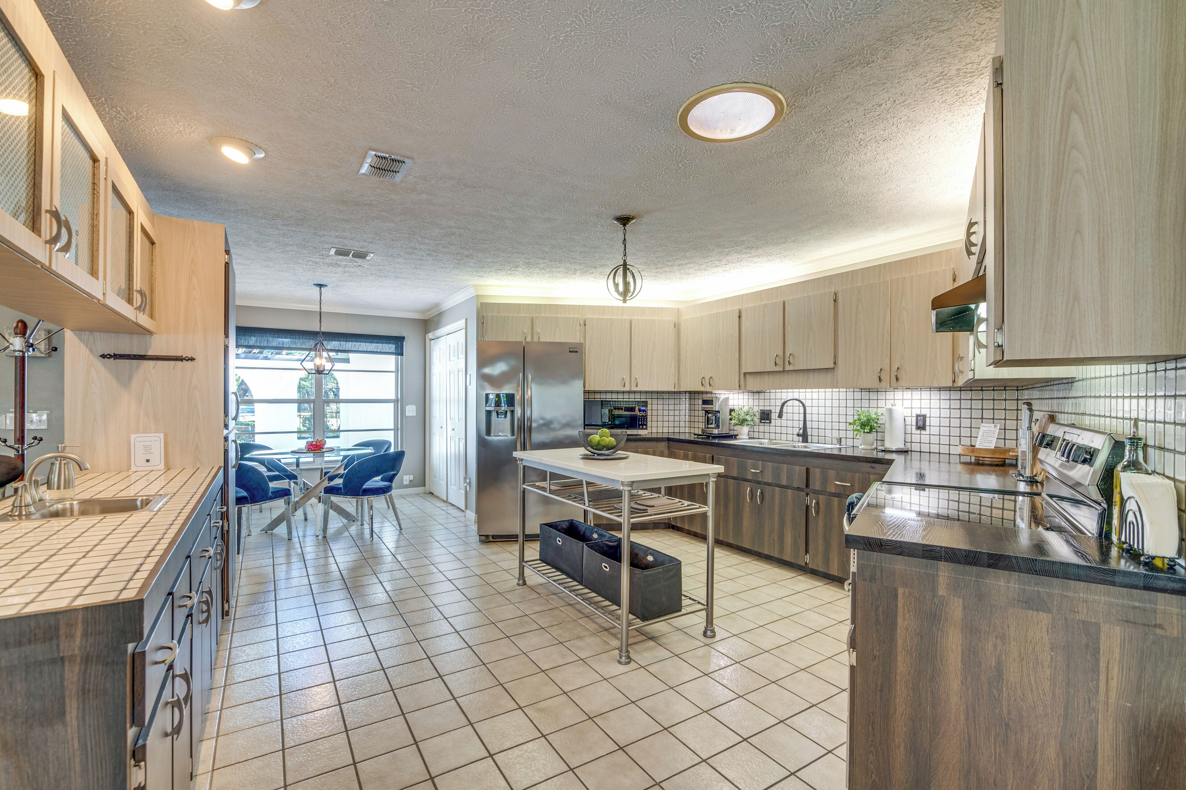 A modern kitchen with a central island, stainless steel appliances, and a dining area with blue chairs.