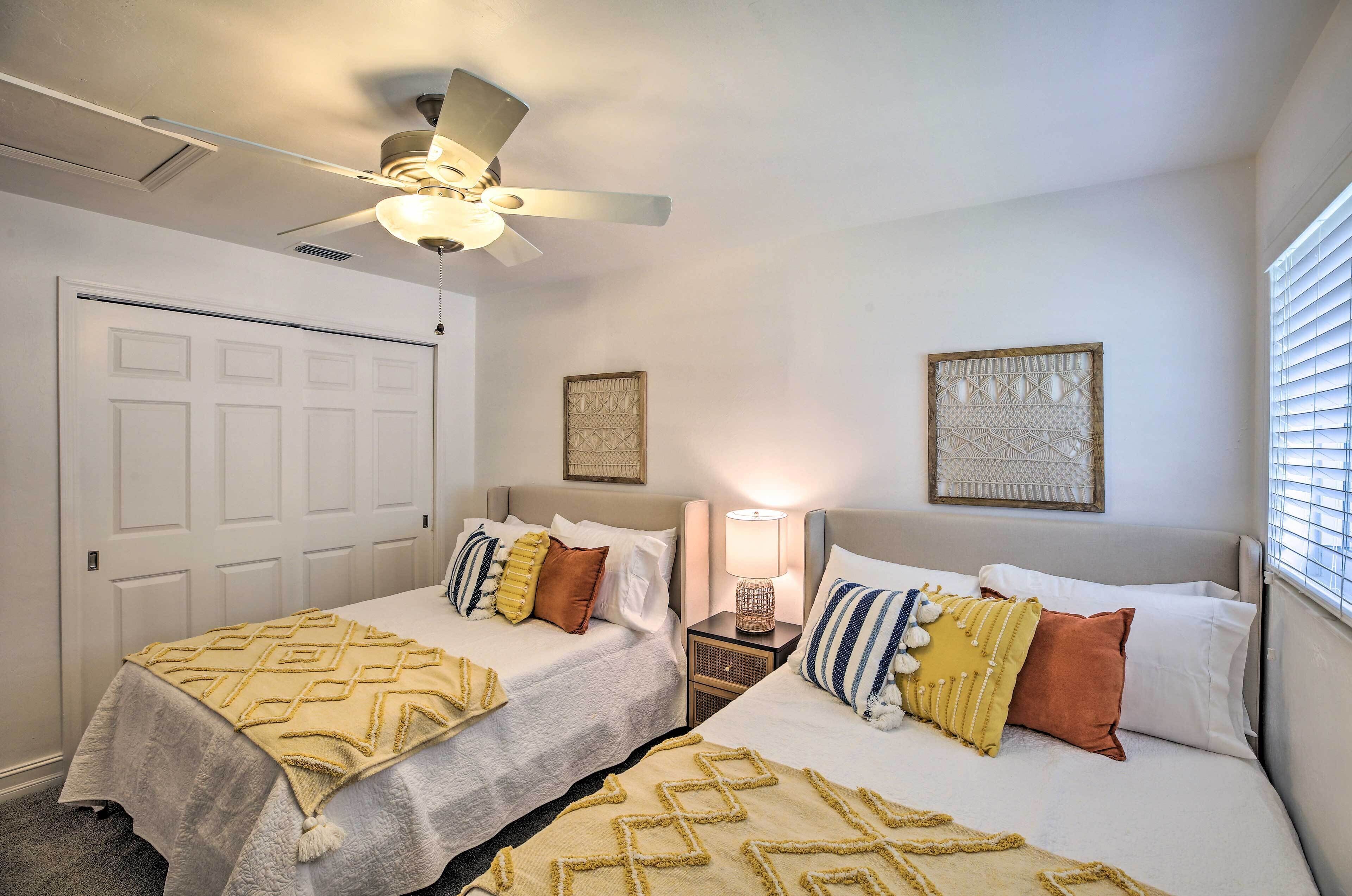 A bedroom with two beds, a ceiling fan, a nightstand with a lamp, and a door.