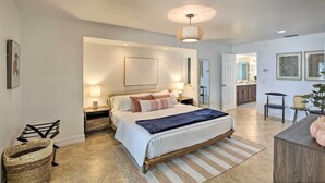 Een ruime slaapkamer met een groot bed, bedlampjes, een houten nachtkastje en een vloerlamp van geweven materiaal.