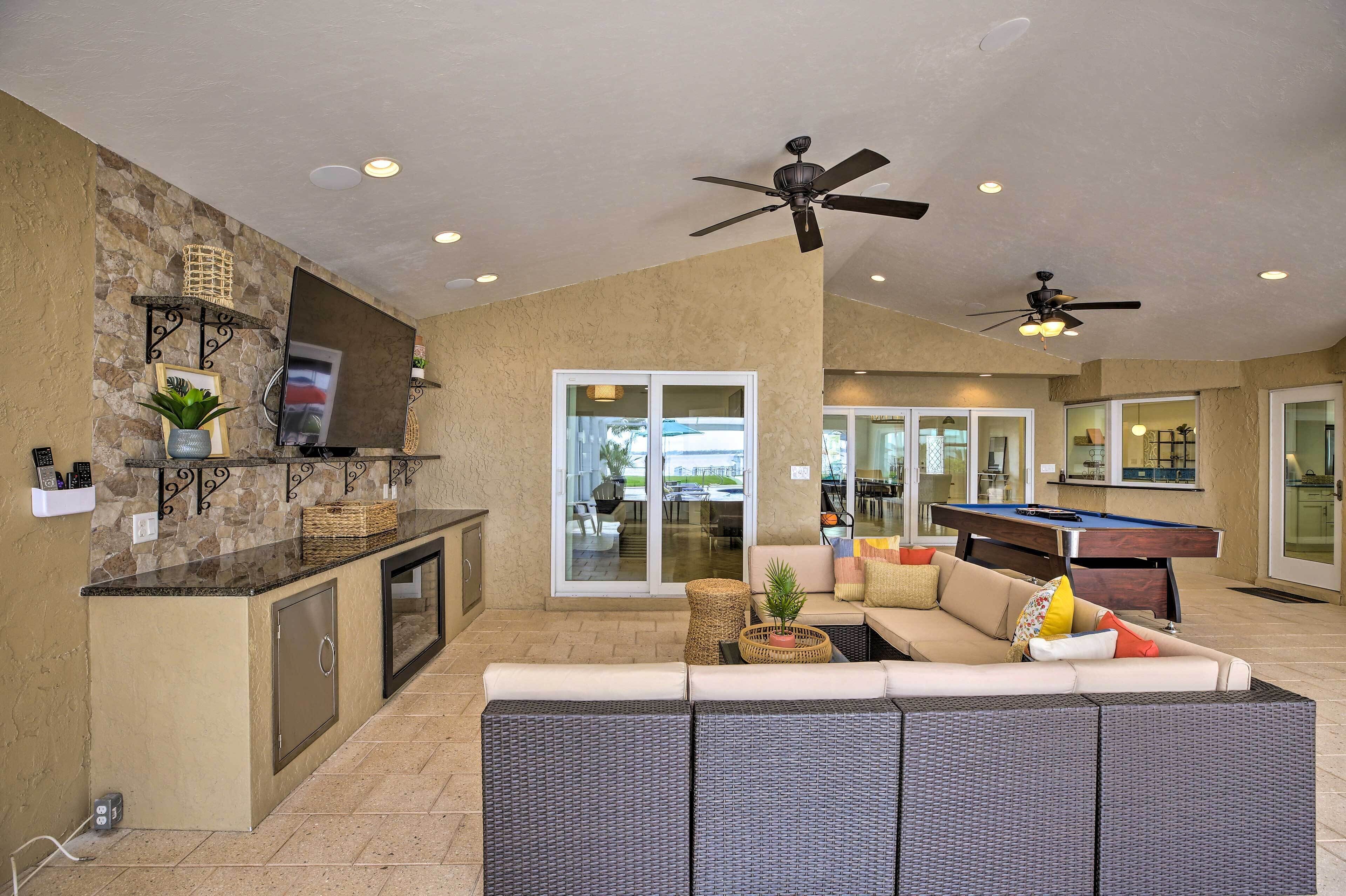 A spacious living area with a pool table, comfortable seating, and a kitchen area with a stone backsplash.