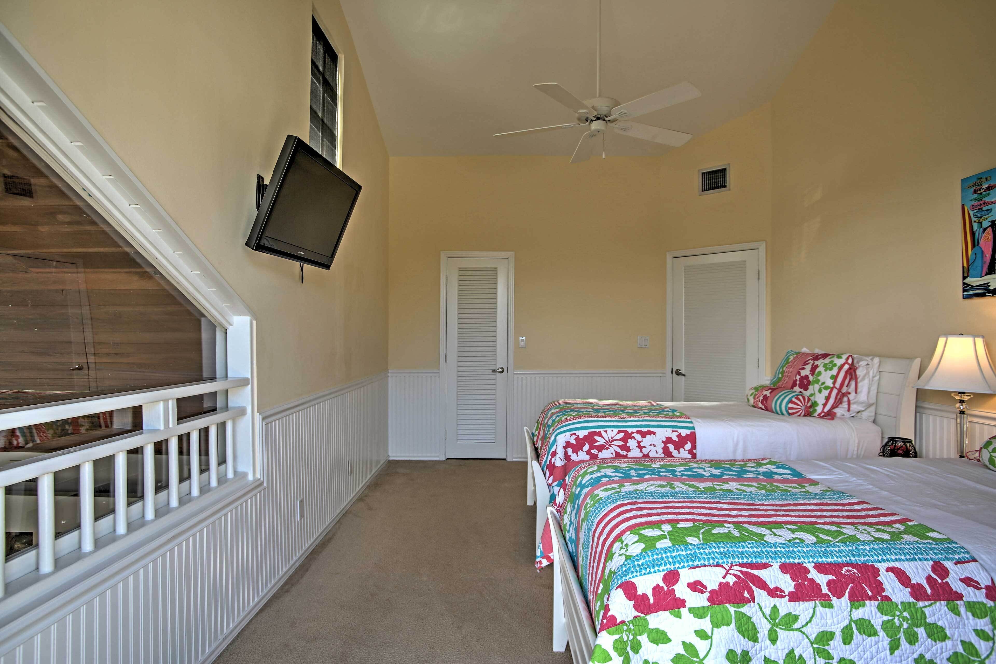 Une chambre avec deux lits, un ventilateur de plafond, une télévision et une porte.