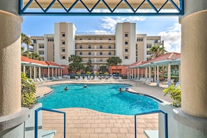 A swimming pool with lounge chairs and umbrellas, surrounded by a building with multiple floors and balconies. - Luxury New Smyrna Beach Condo w/ Resort Amenities! (New Smyrna Beach)