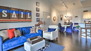 A modern living room with a blue sofa, white armchairs, and a dining area with blue chairs.