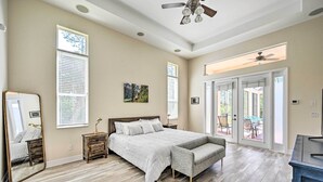 Quarto com cama grande, um banquinho, cômoda, espelho e ventoinha no teto.