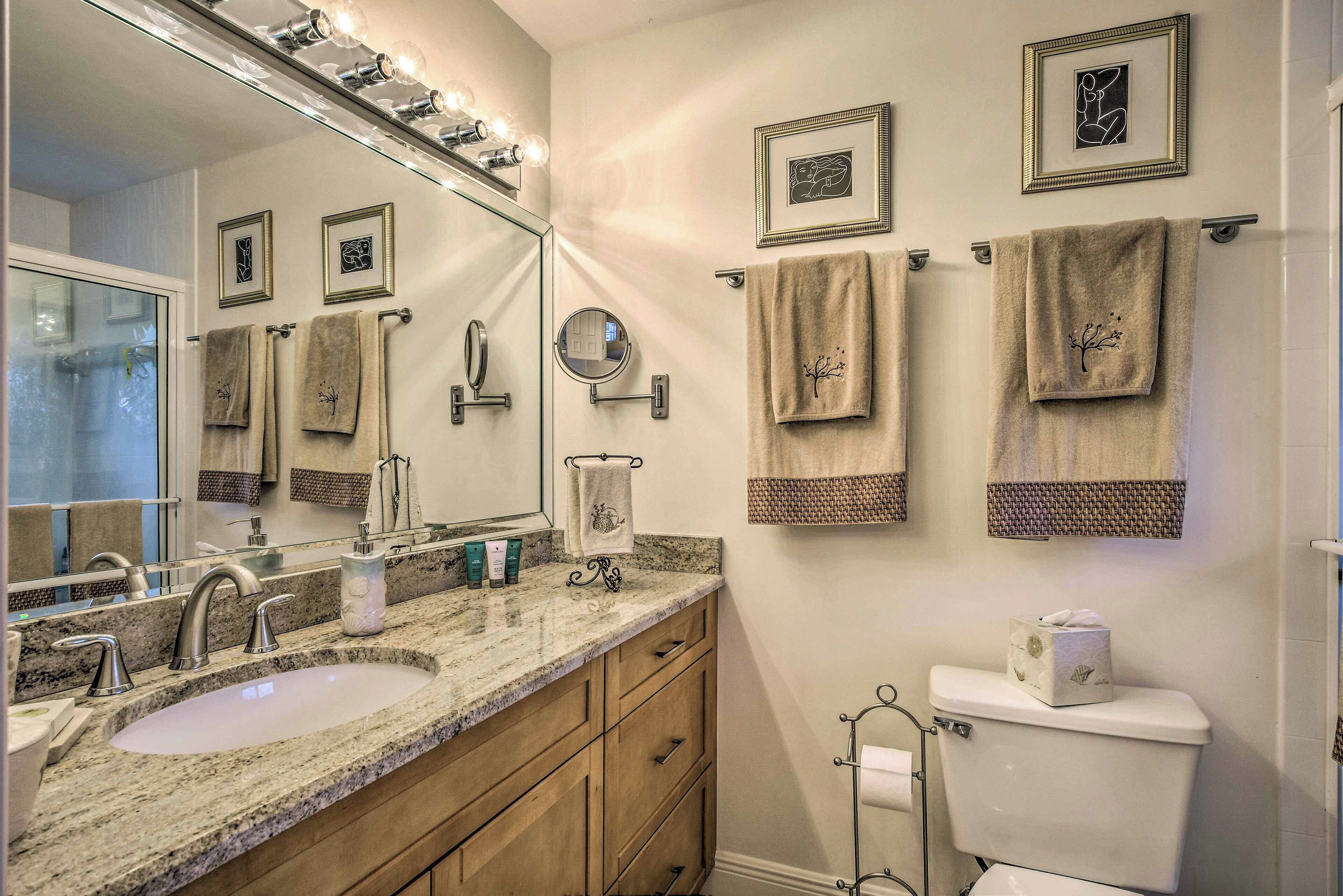 A bathroom with a granite sink, a large mirror, and multiple towels on the wall.