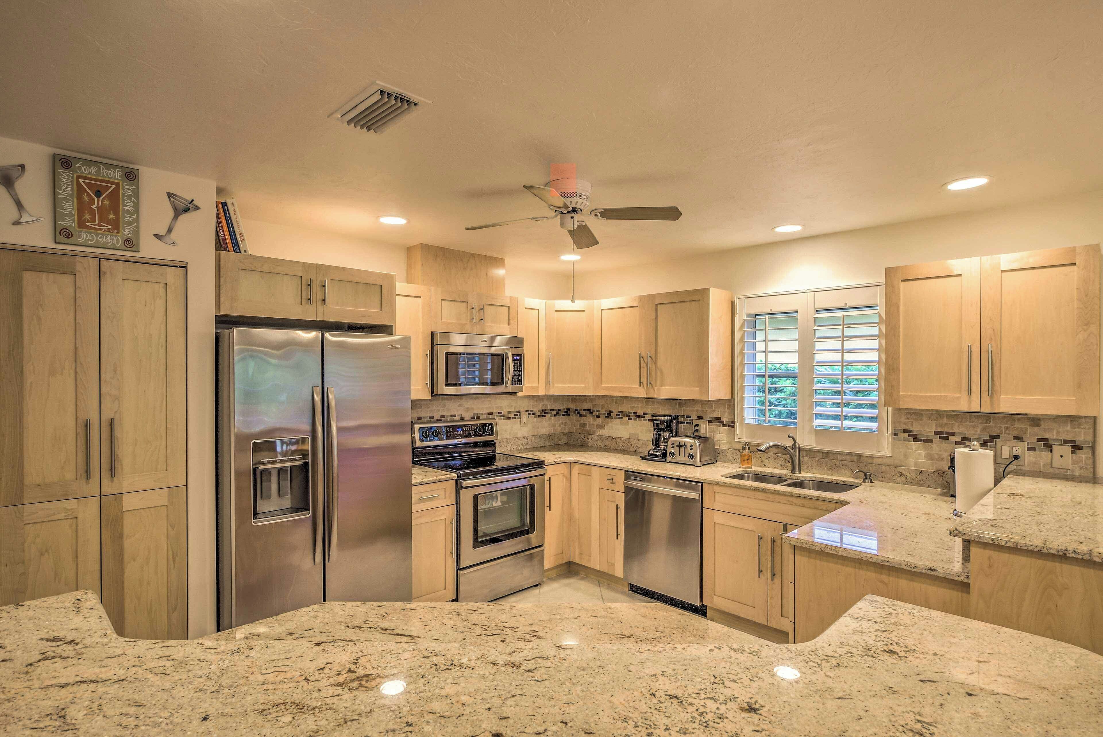 A modern kitchen with granite countertops, stainless steel appliances, wooden cabinets, and a ceiling fan.