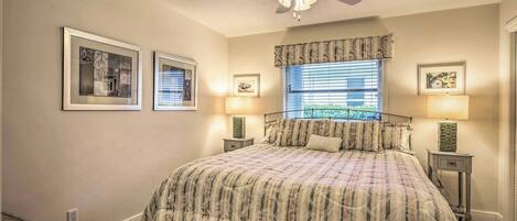 A bedroom with a large bed, a ceiling fan, two bedside lamps, and framed artwork on the walls.