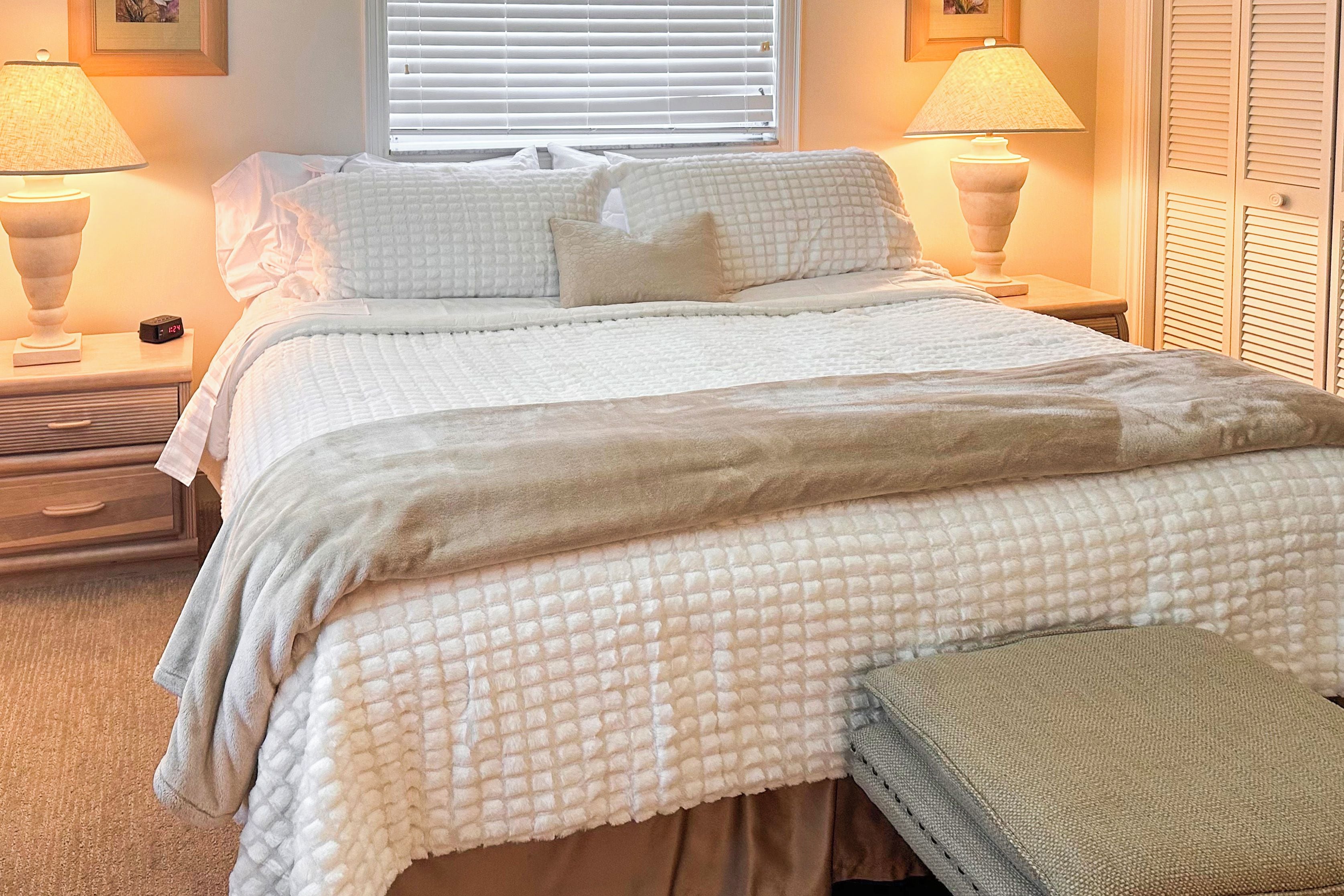 A neatly made bed with a quilted duvet, two bedside lamps, and a clock on the nightstand.
