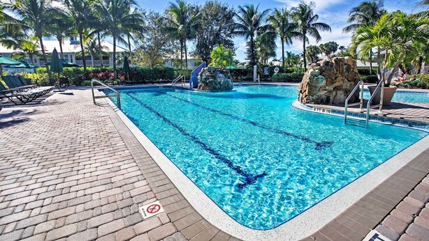 A clear blue pool with a stone feature, surrounded by palm trees and lounge chairs. - Free Golf Until Oct! Naples Condo w/ Resort Pool (Naples)