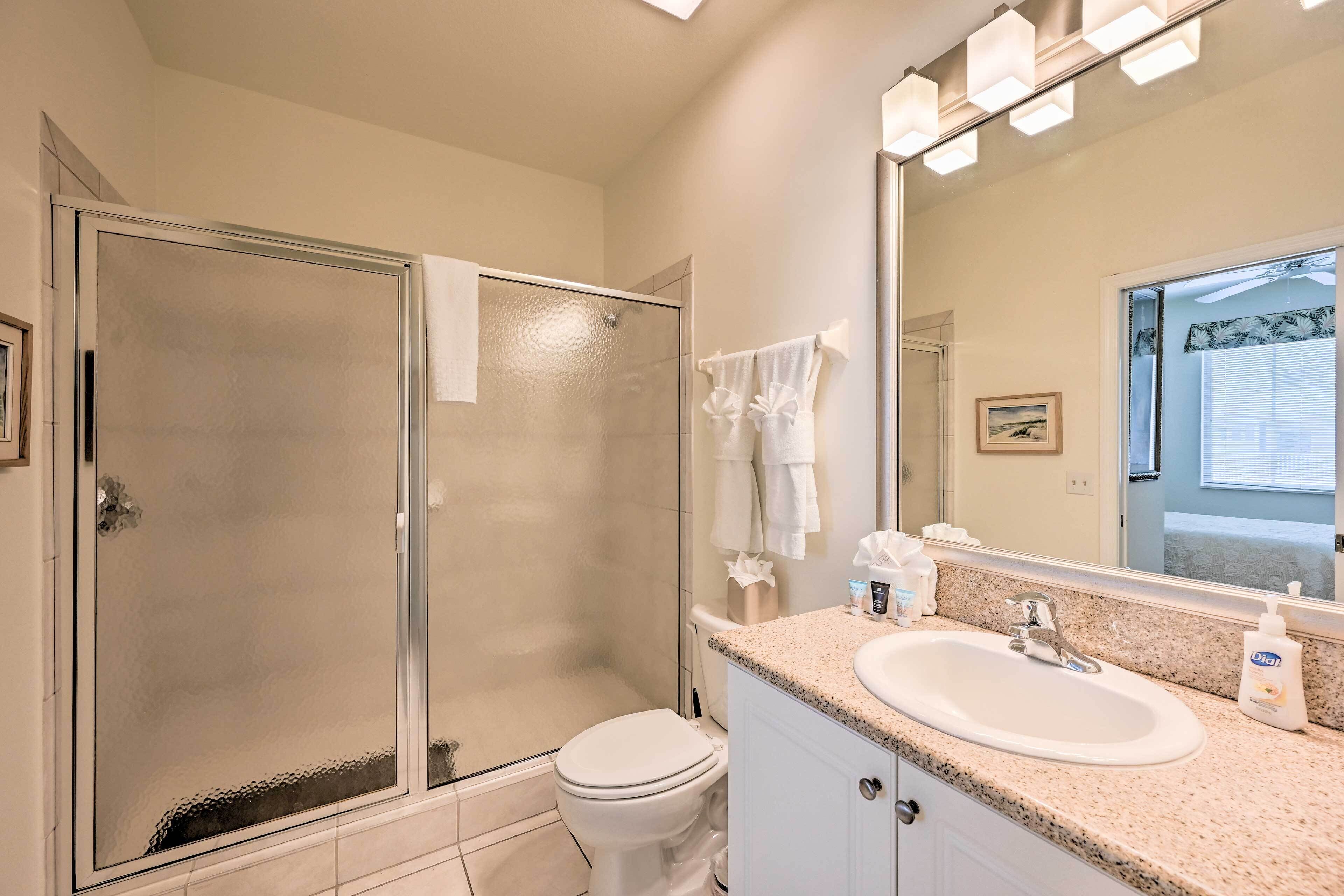 A bathroom with a glass-enclosed shower, a white toilet, a sink with a mirror, and a countertop with toiletries.