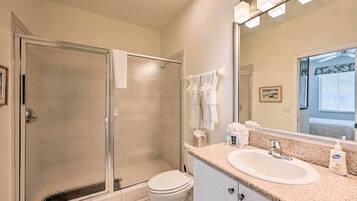 A bathroom with a glass-enclosed shower, a white toilet, a sink with a mirror, and a countertop with toiletries.