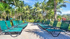 A row of green lounge chairs on a paved walkway surrounded by palm trees. - Free Golf Until Oct! Naples Condo w/ Resort Pool (Naples)
