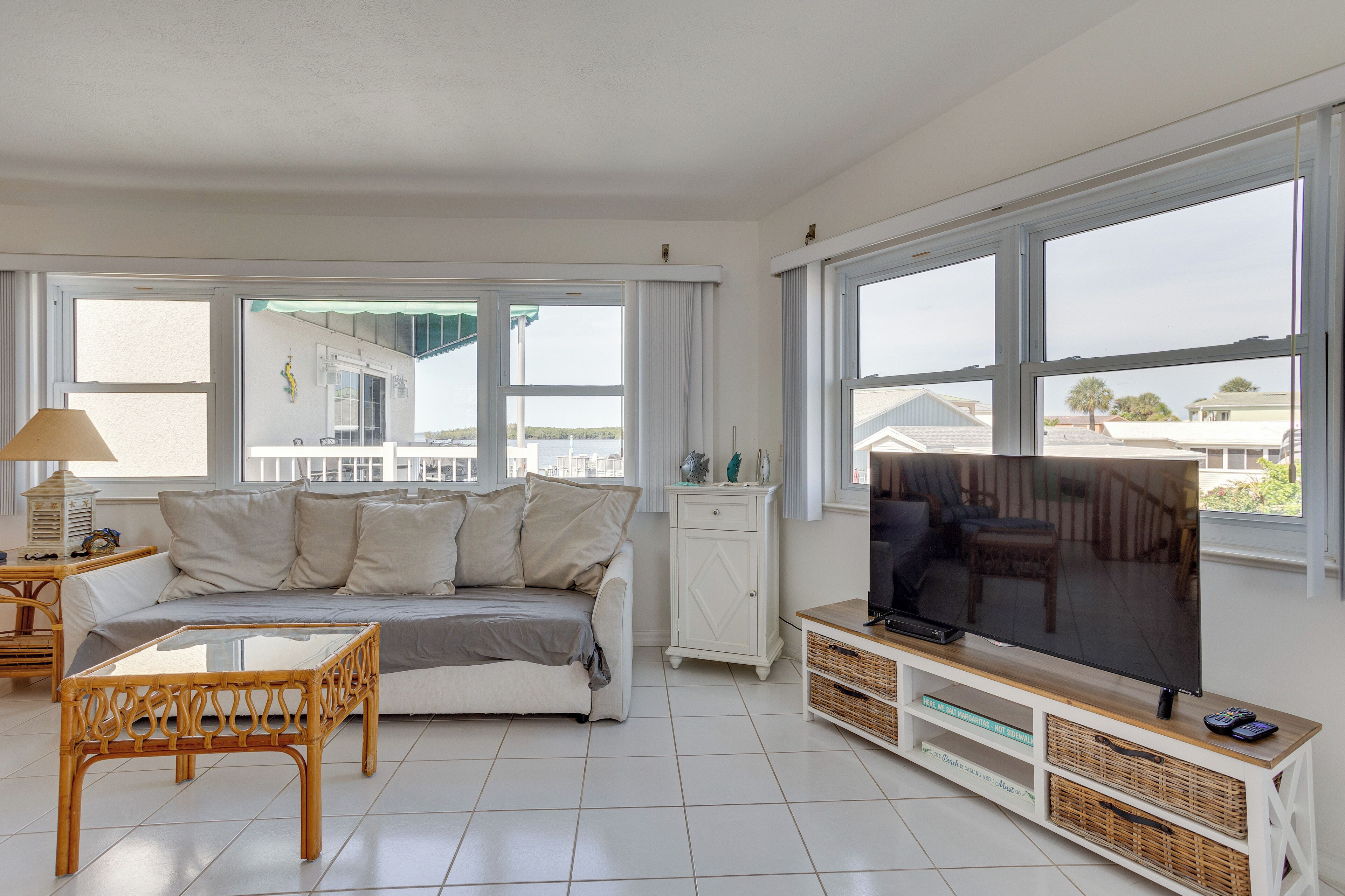 A living room with a sofa, a glass coffee table, a TV on a wooden stand, and large windows with a view of buildings.