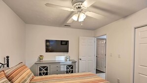 Un dormitorio con una cama, un aparador, un ventilador de techo y un televisor en la pared.