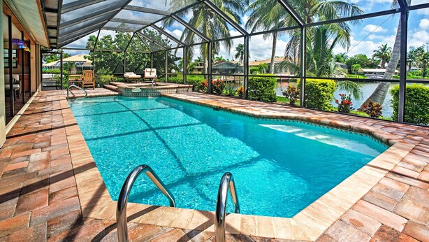 A swimming pool with a glass enclosure, surrounded by palm trees and a view of the water.