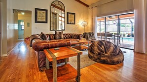 A spacious living room with a leather sofa, a coffee table, and a bean bag chair. There is a large mirror on the wall and a door leading to another room.