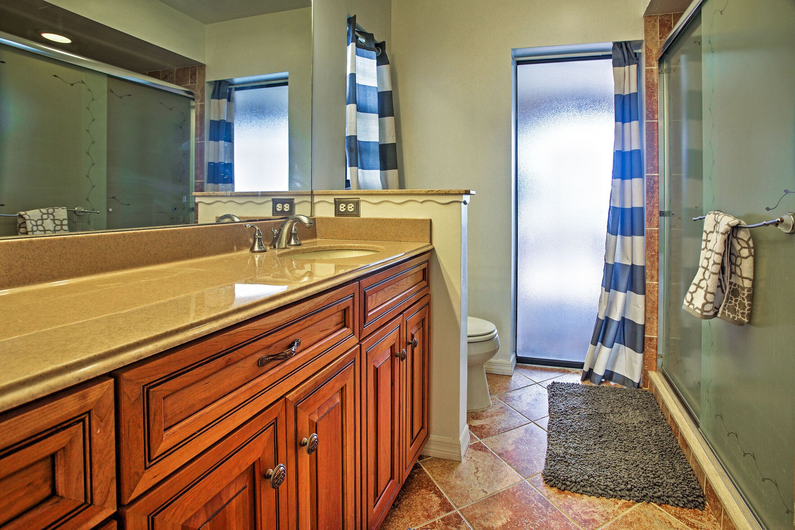 Une salle de bain avec un grand meuble-lavabo en bois, un évier, un miroir, des toilettes et une douche dotée d’un rideau à rayures.