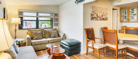 A living room with a sofa, ottoman, wooden coffee table, and dining table with chairs.