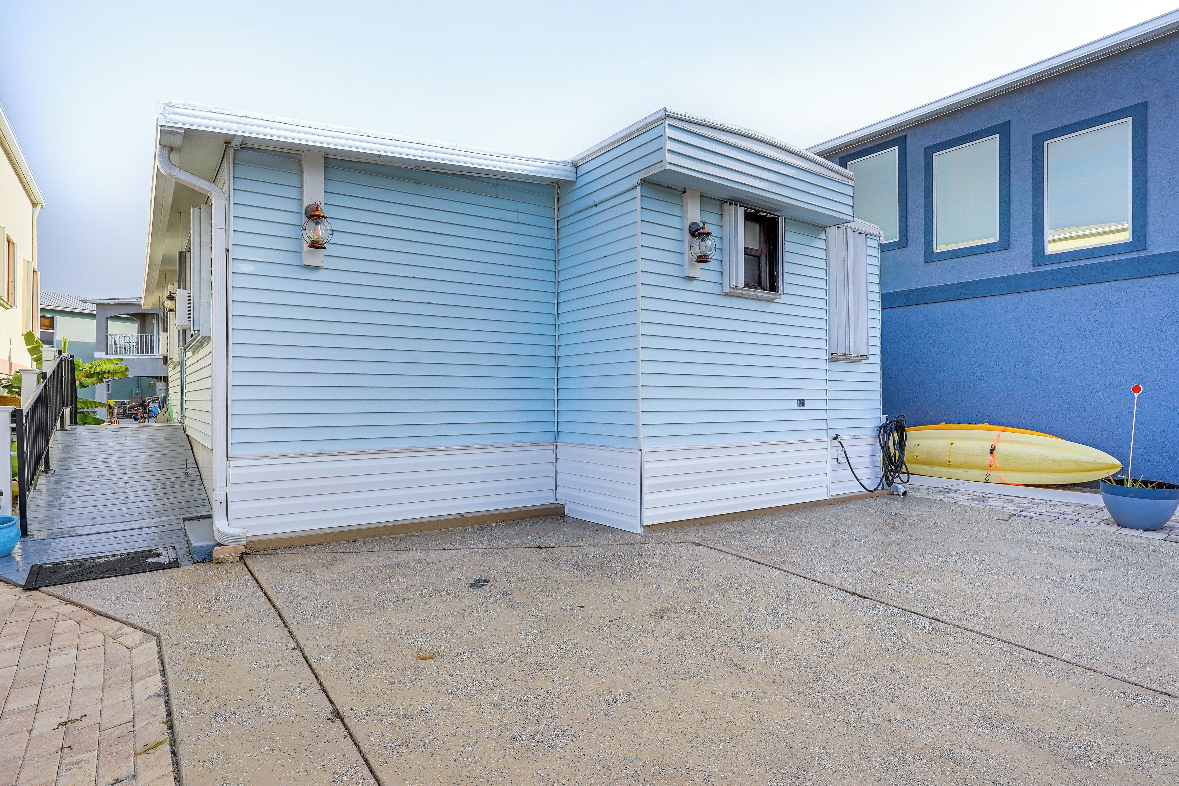 A corner building with light blue siding, a small window, and a yellow surfboard leaning against the wall.