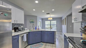 Una cocina moderna con refrigerador de acero inoxidable, microondas y lavavajillas, un salpicadero de azulejos azules y una ventana con persianas.