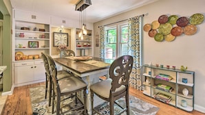 A dining area with a wooden table, chairs, a chandelier, and a bookshelf with decorative items.