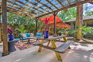 Eine Terrasse im Freien mit einem Holztisch und Bänken, umgeben von Topfpflanzen und einem blauen Sofa.