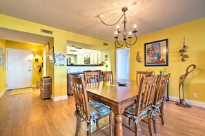 A dining area with a wooden table and chairs, a chandelier, and a kitchen in the background. - Oceanfront Daytona Beach Condo Near Boardwalk! (Daytona Beach)
