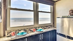 Cucina con vista sull'oceano attraverso un'ampia finestra, un frigorifero in acciaio inossidabile e un cartello di benvenuto.