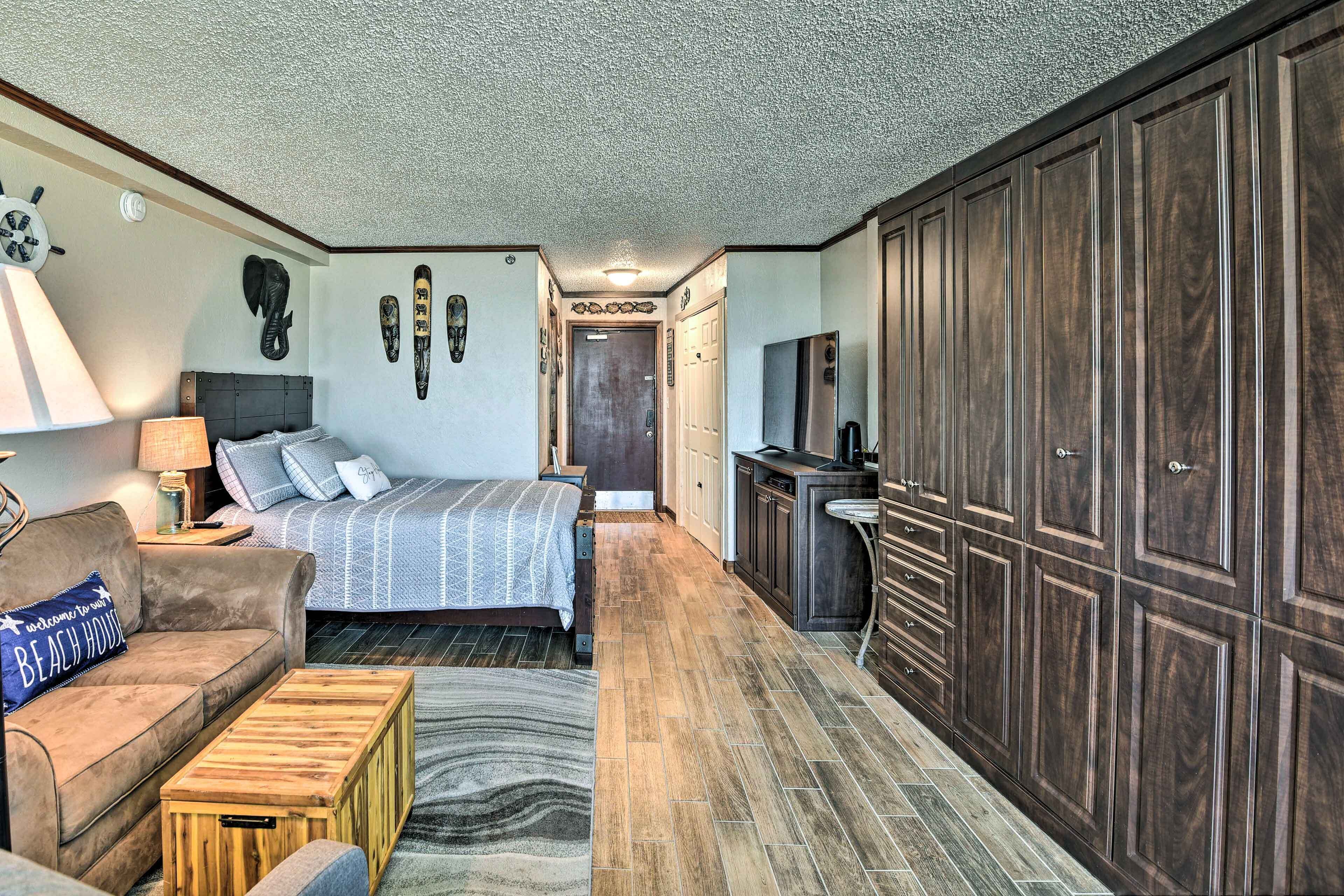 A compact bedroom with a bed, a sofa, a wooden coffee table, and a wardrobe.