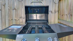 Una parrilla de gas portátil con tres perillas de control y una pantalla digital, sobre un fondo de valla de madera.