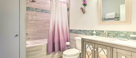 A bathroom with a shower, toilet, vanity, and a mirror.