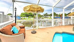 A covered outdoor area with a pool, a wicker sofa with cushions, a thatched umbrella, and a metal railing. - 'ocean Breeze Oasis' w/ Boat Dock & Slip on Canal! (Bradenton)